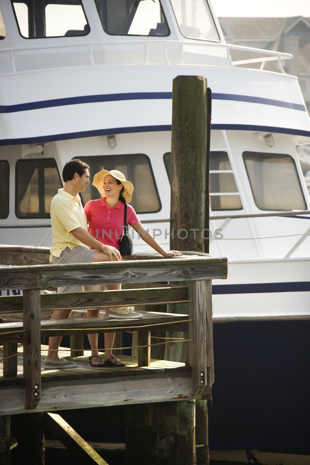 Mid-adult Caucasian couple at dock looking at each other with boat in background.