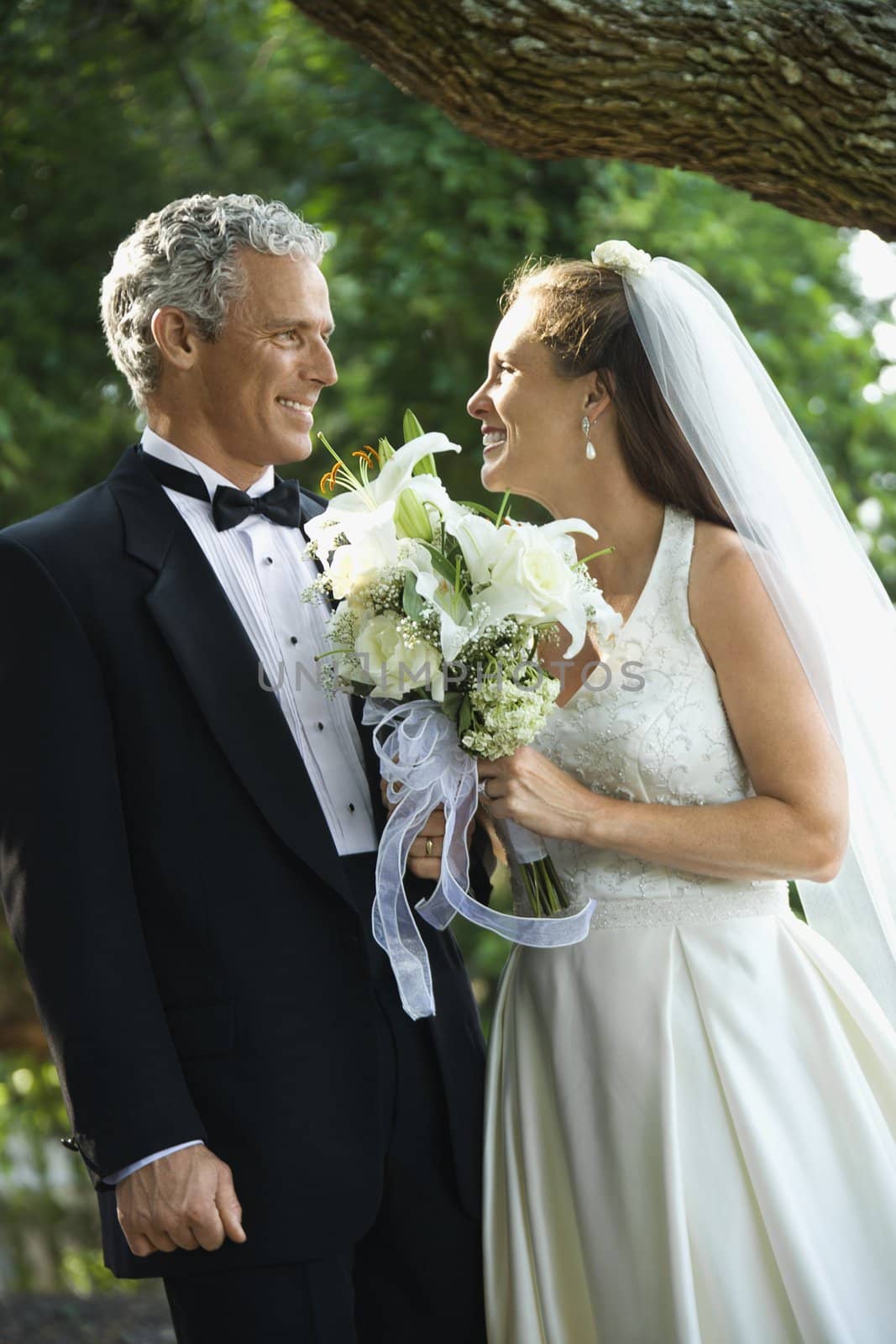 Portrait of a bride and groom smiling at each other outside.