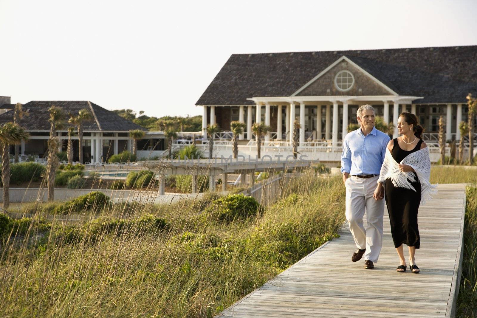 Caucasian mid-adult couple walking on walkway near beach home.