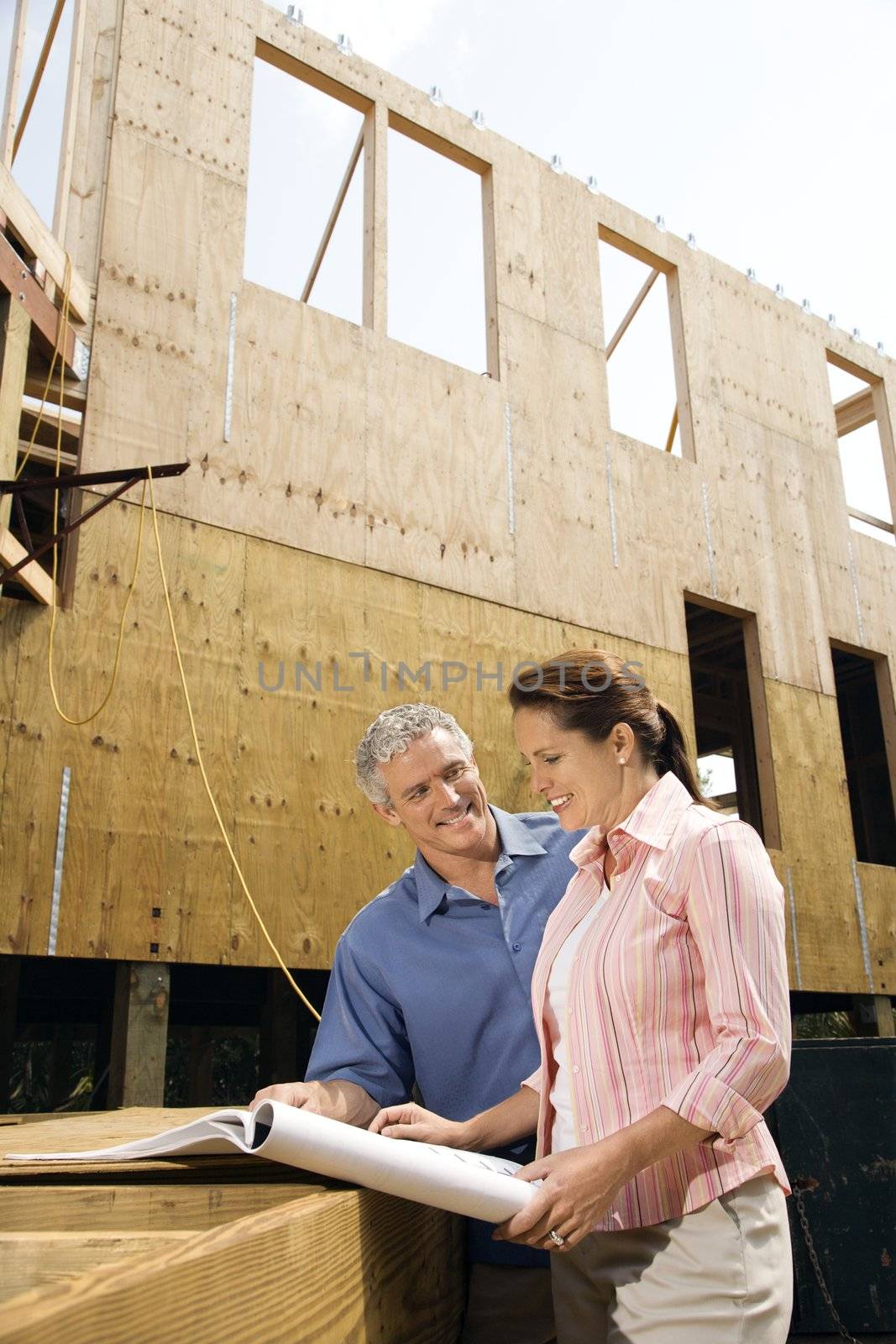 Caucasian mid-adult male and female looking at blueprints in construction phase of house.