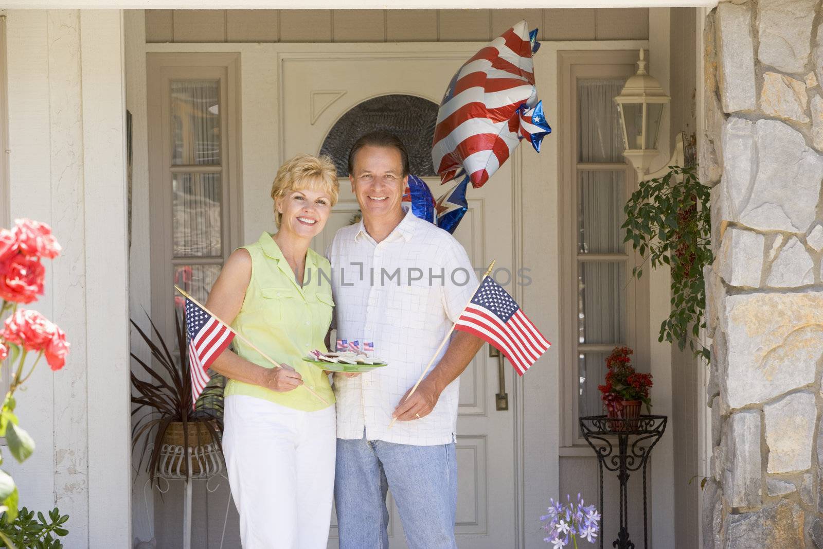 Couple at front door on fourth of July with flags and cookies sm by MonkeyBusiness