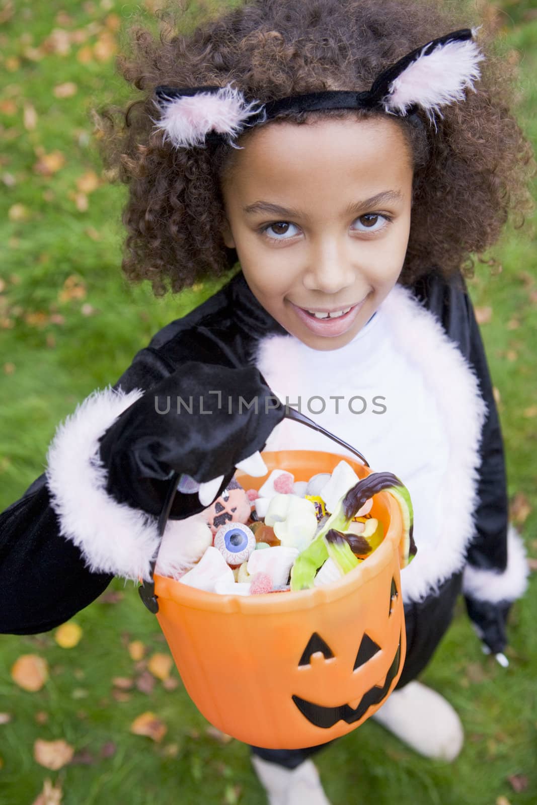 Young girl outdoors in cat costume on Halloween holding candy by MonkeyBusiness