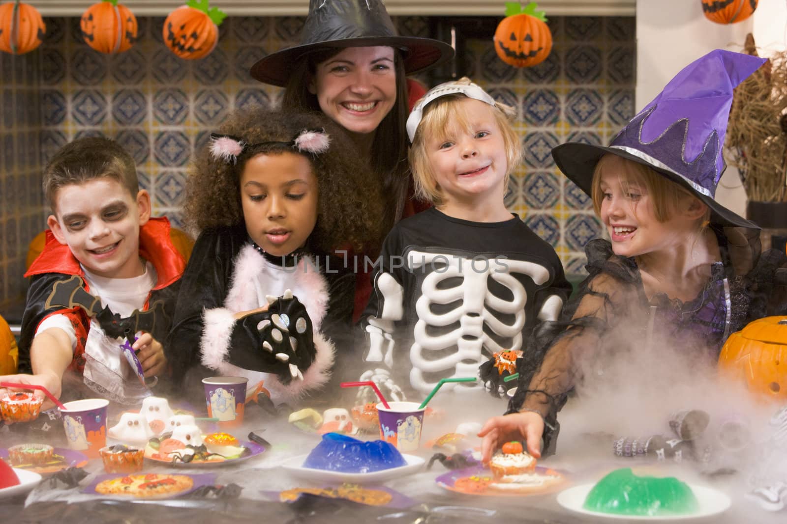 Four young friends and a woman at Halloween eating treats and sm by MonkeyBusiness