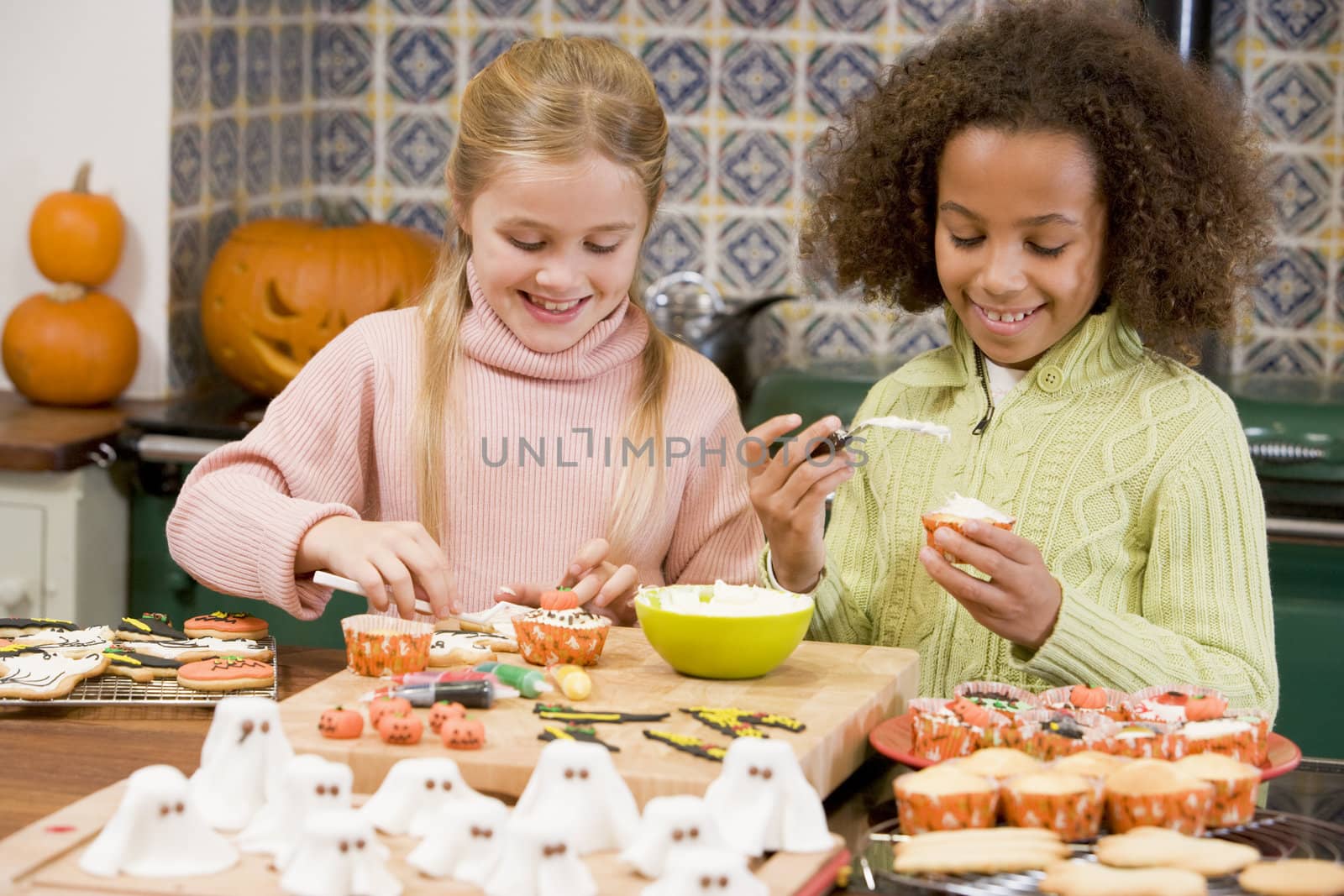 Two young girl friends at Halloween making treats and smiling by MonkeyBusiness