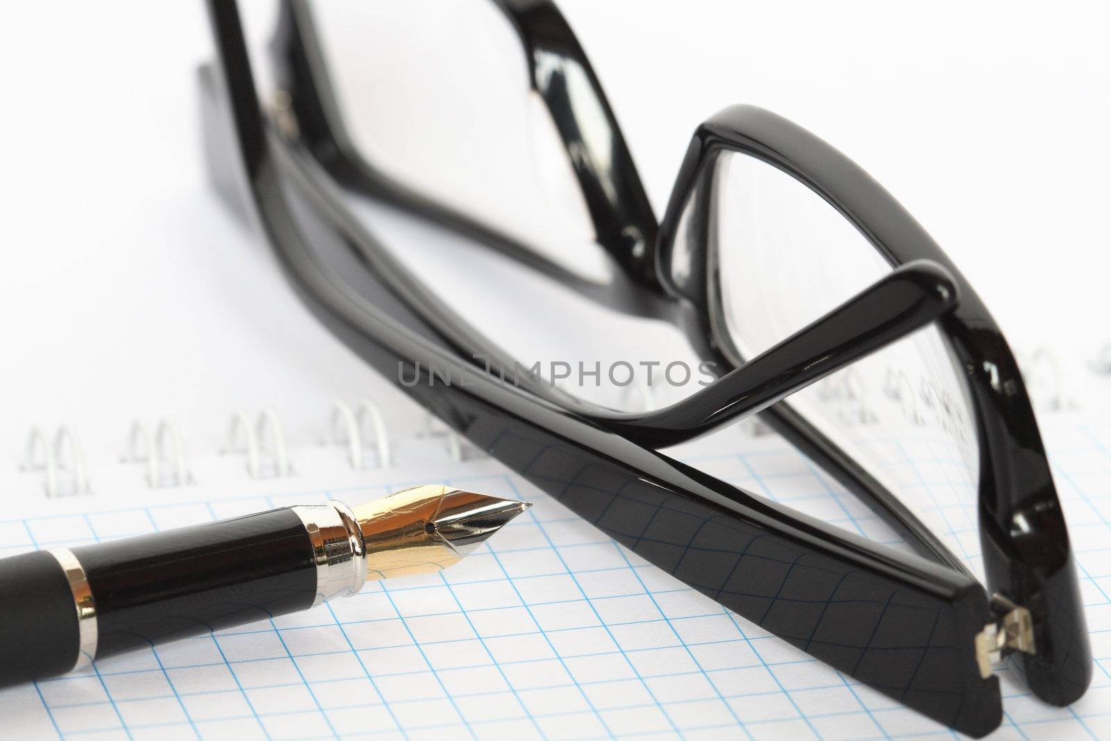 Closeup of fountain pen and  black spectacles lying on open spiral notebook