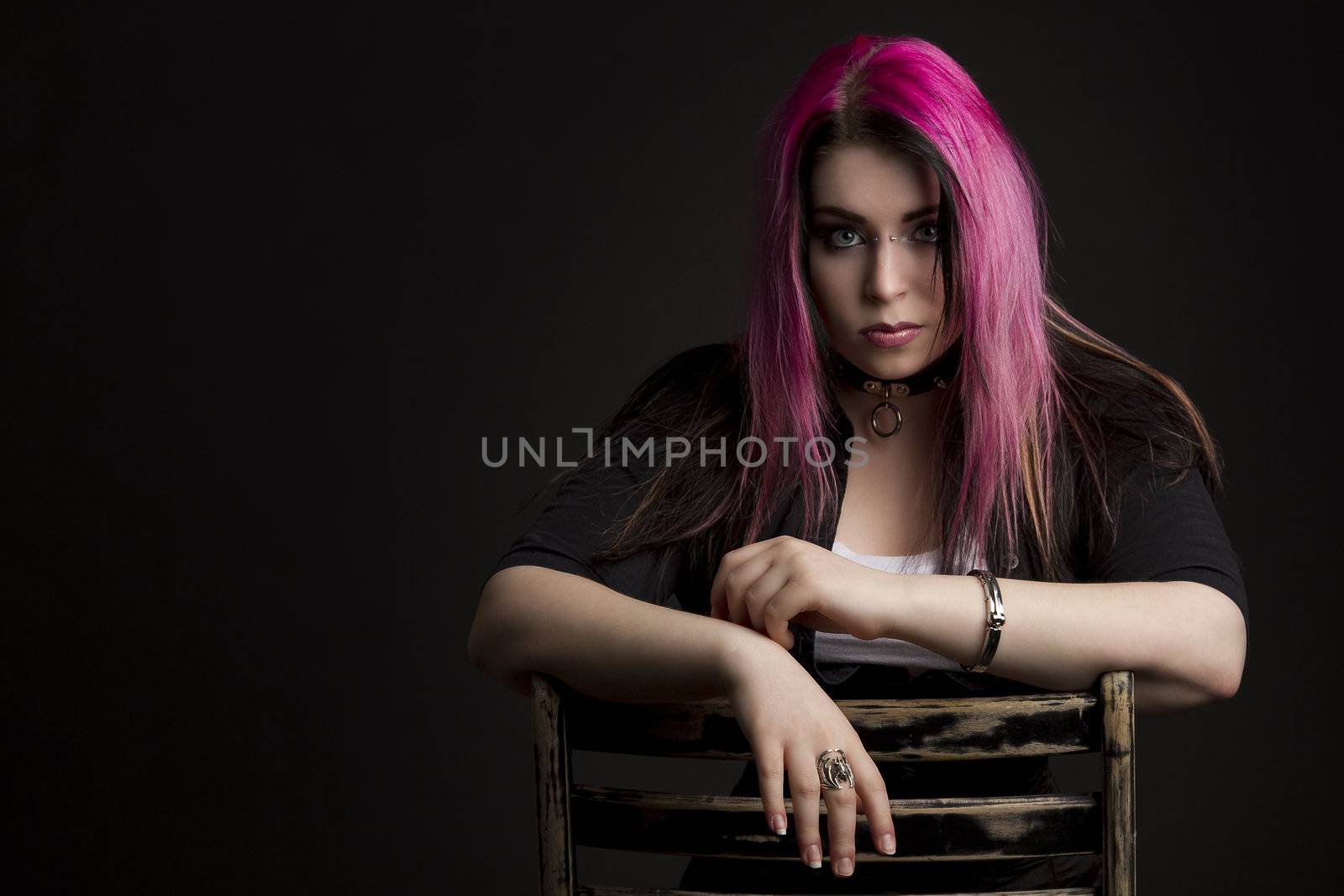 Goth girl with pink hair and body piercing sitting on chair
