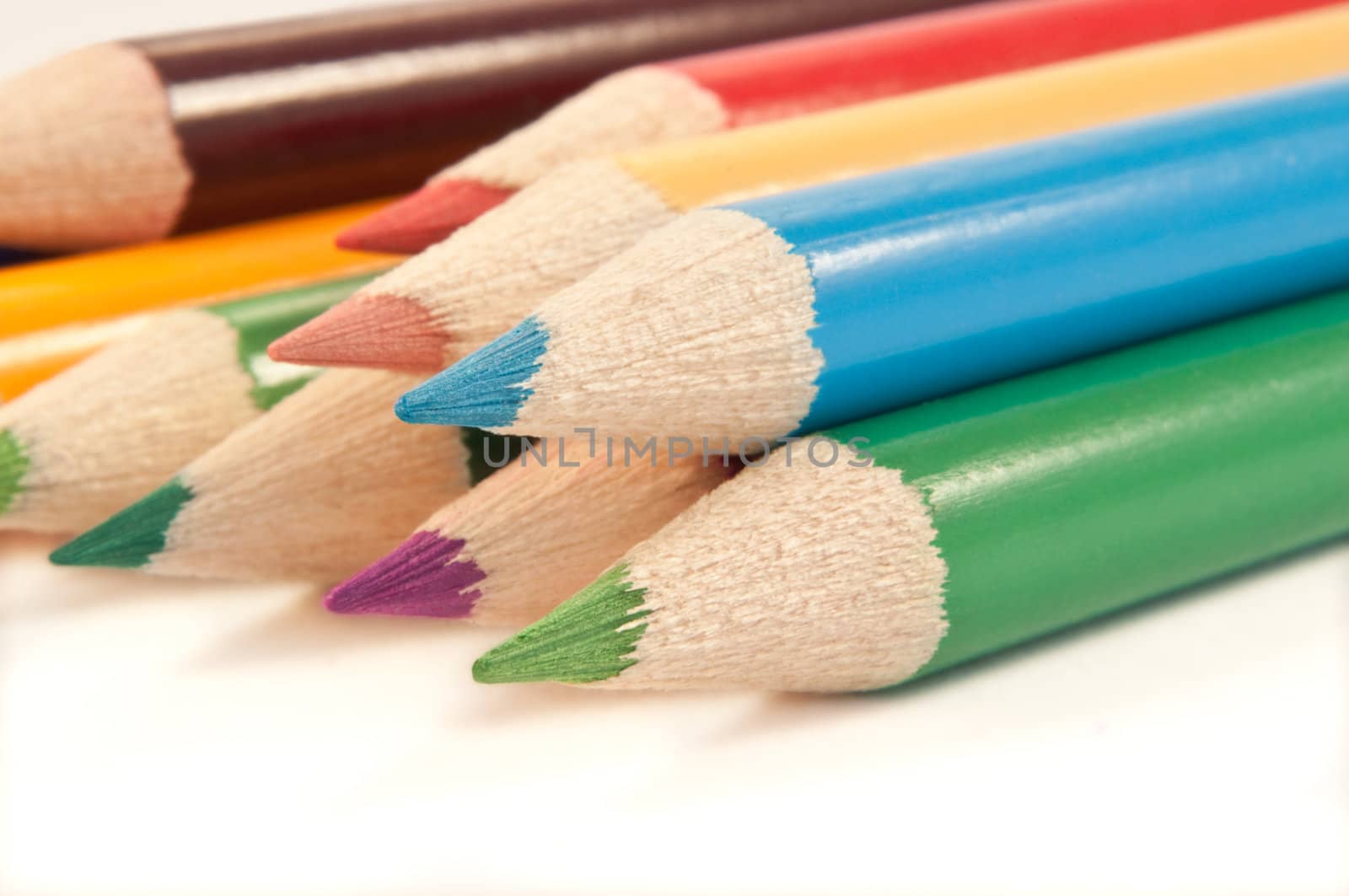 Close up capturing a selection of coloured drawing pencils arranged over white.