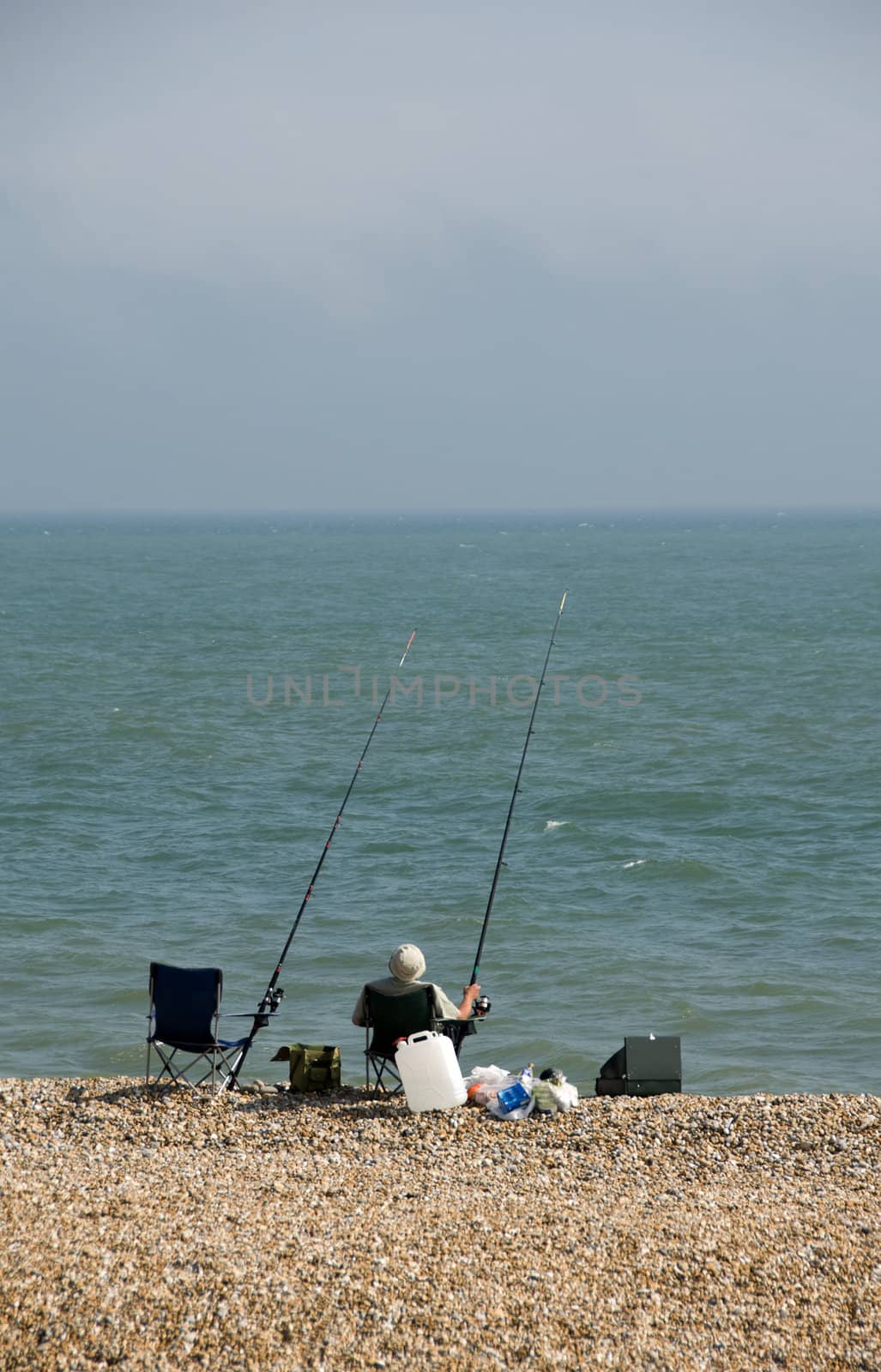 A man sea fishing on a pebble beach