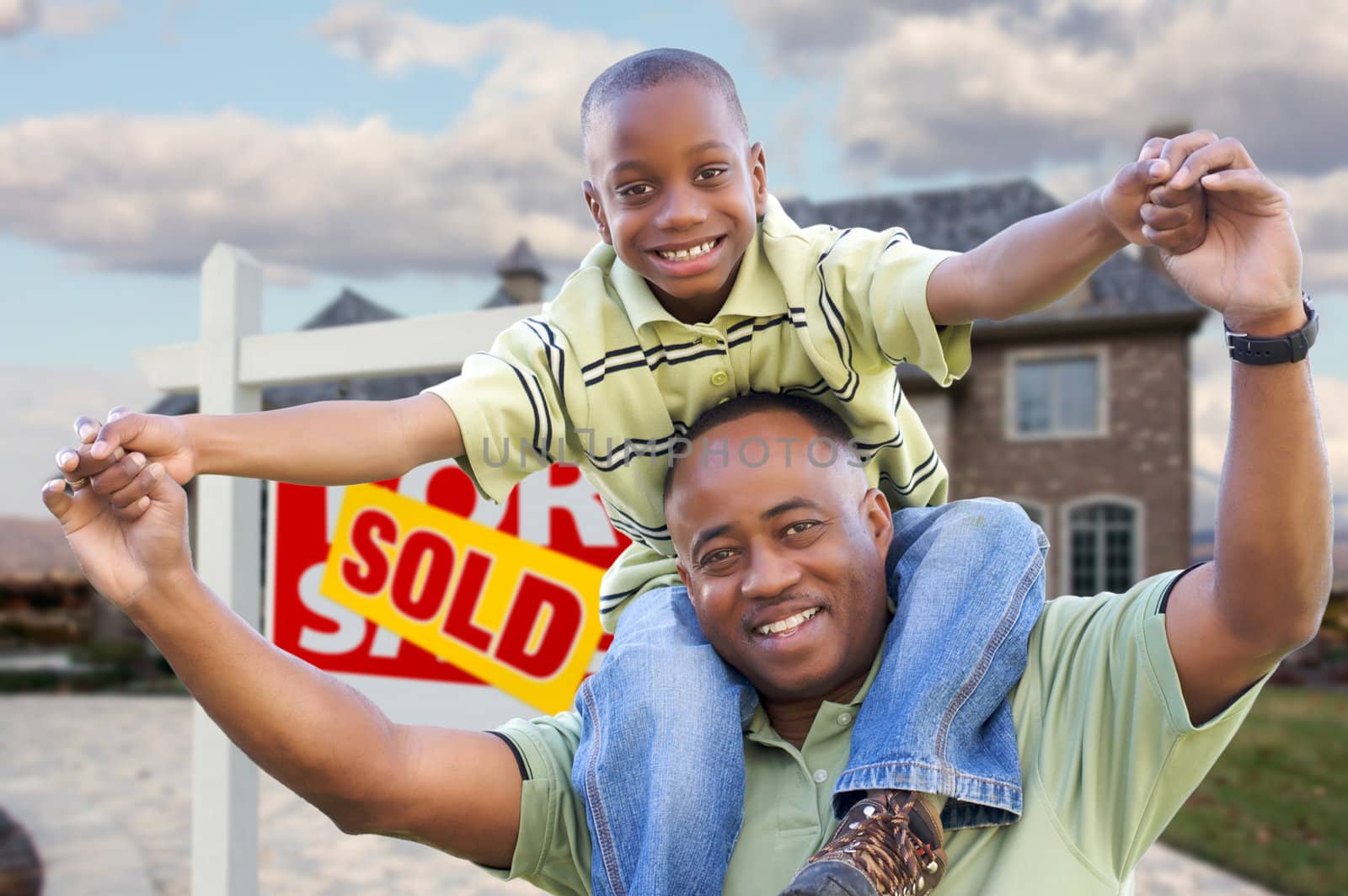 Happy African American Father and Son in Front of New Home and Sold Real Estate Sign.