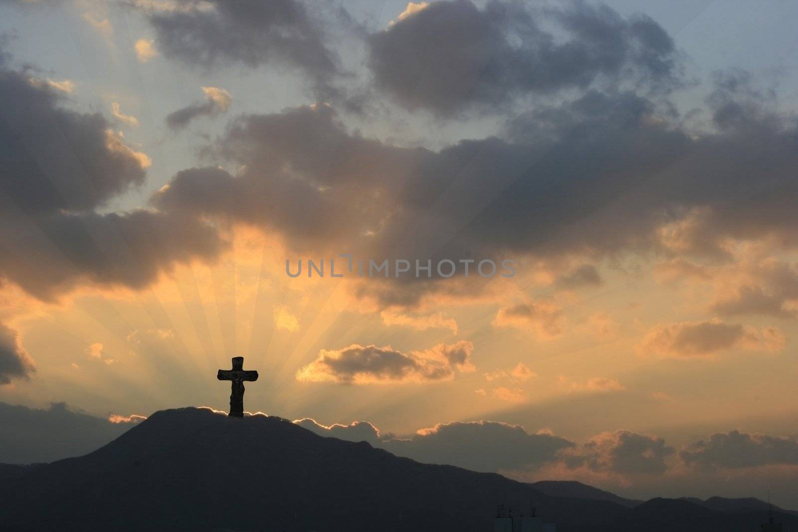 Cross on Dramatic Sunset in a beautiful landscape-mountain and sunbeams rays accentuating through thick clouds.