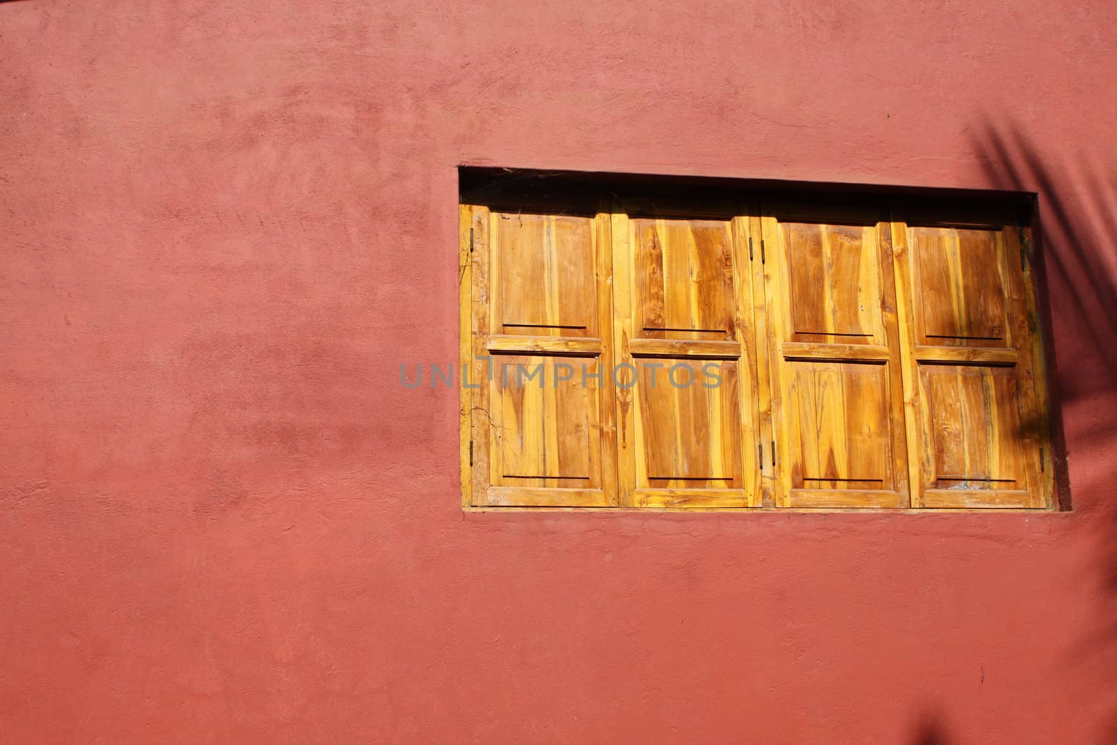 A closed wooden window on a red wall.