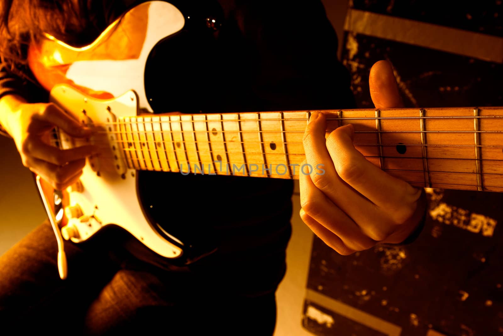 Musician playing guitar at studio with shallow depth of field and orange lighting. 