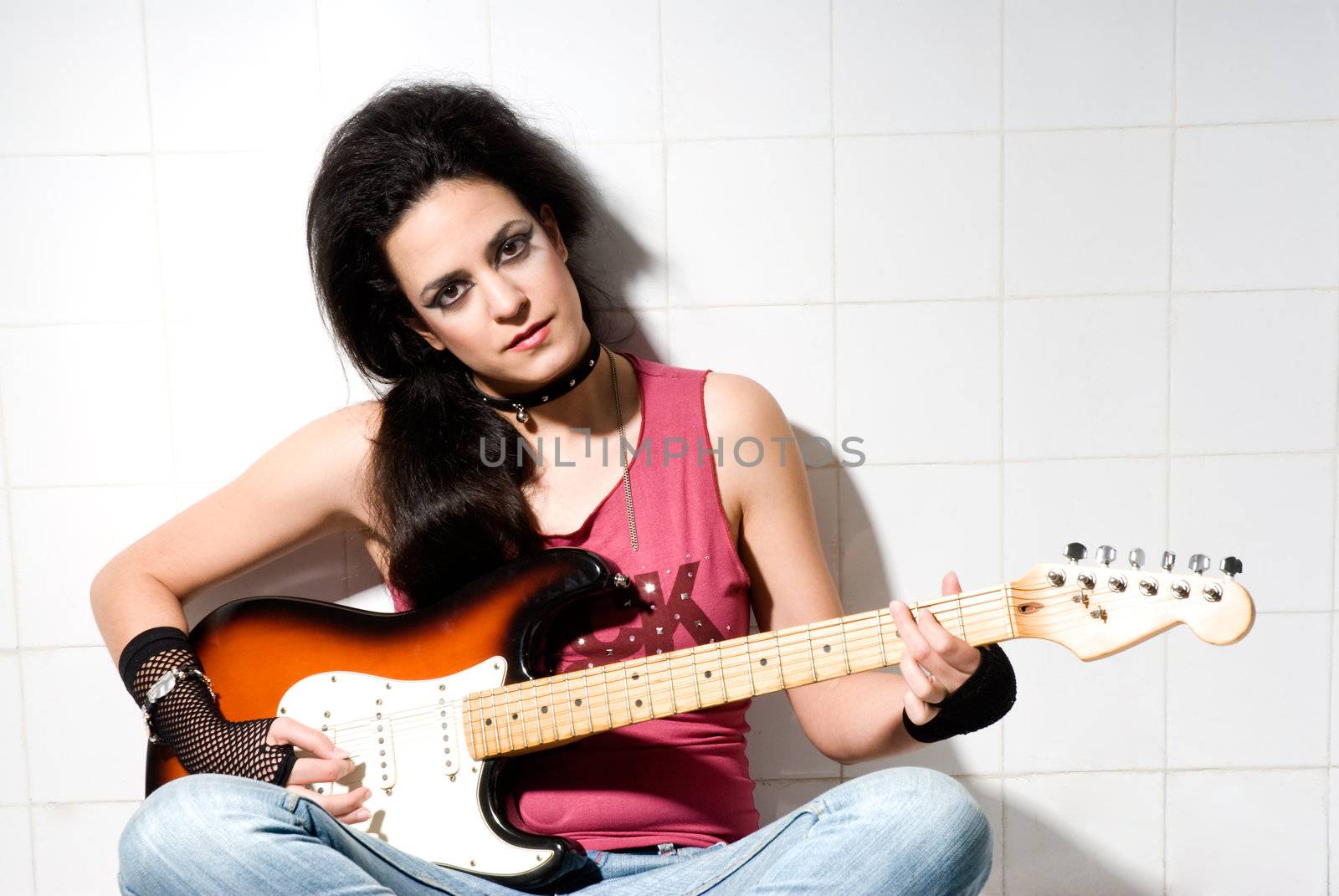 Punk female playing electric guitar on underground background. 
