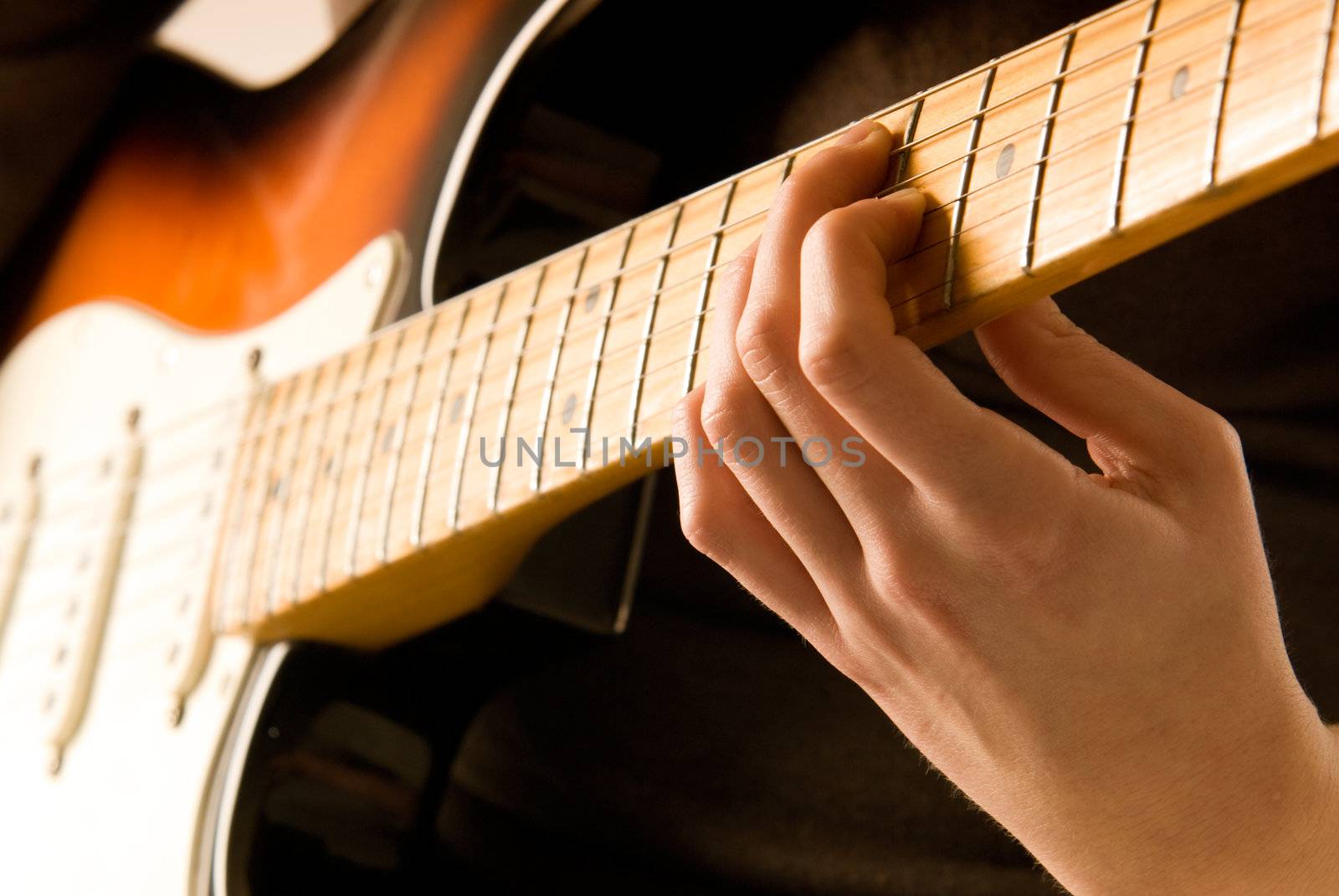 Hand playing guitar chord with shallow depth of field and soft orange tone. 