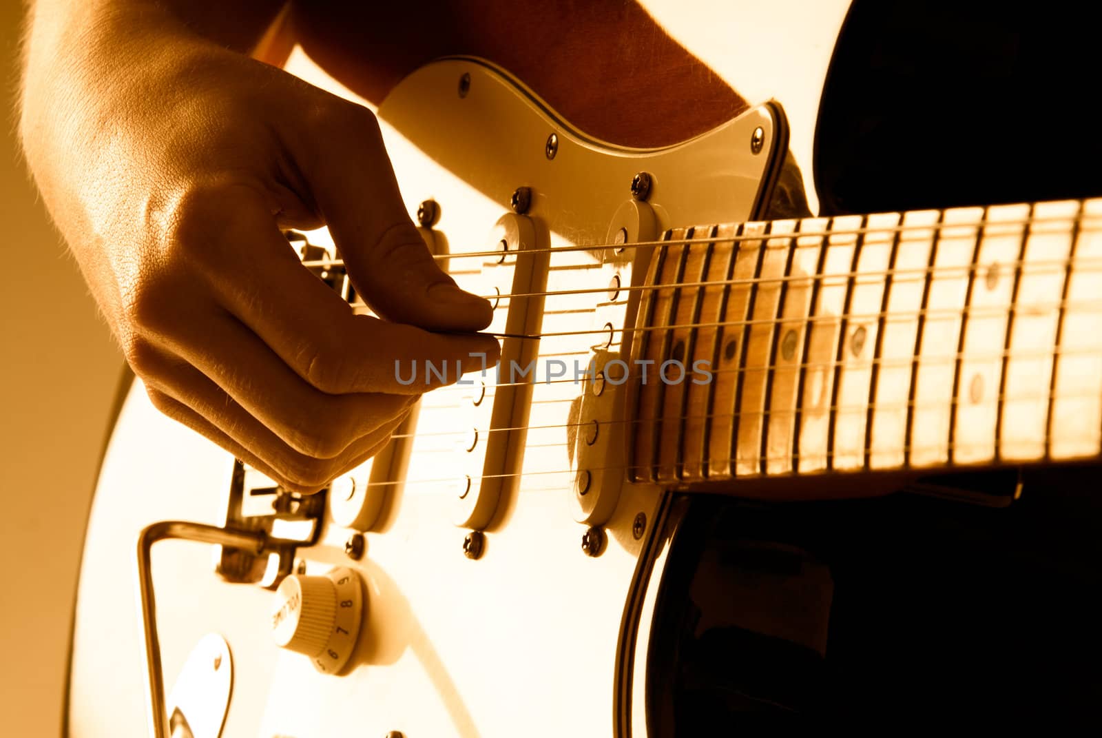 Hand picking guitar strings with shallow depth of field and orange lighting. 