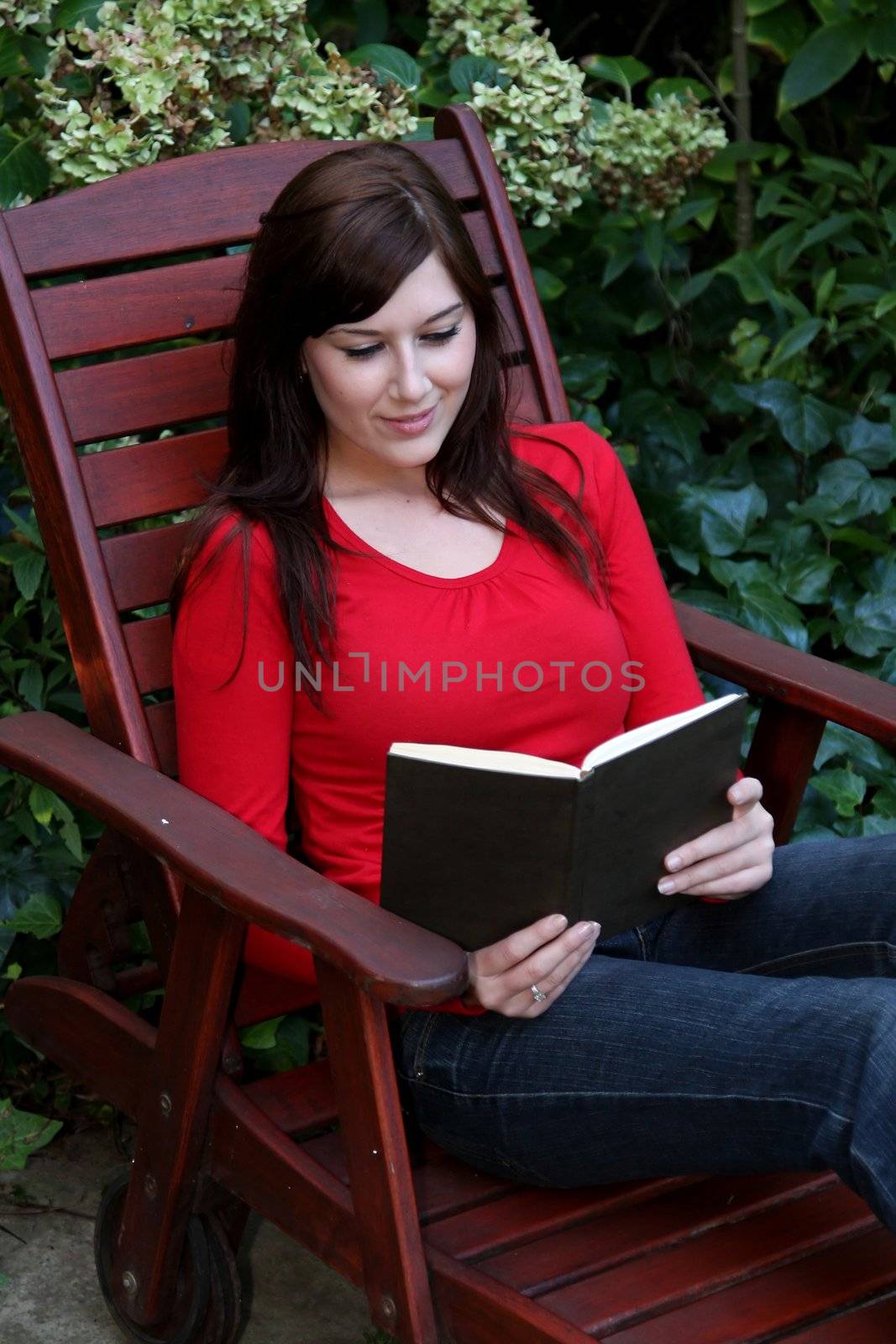 Gorgeous brunette woman on wooden slatted chair reading a book