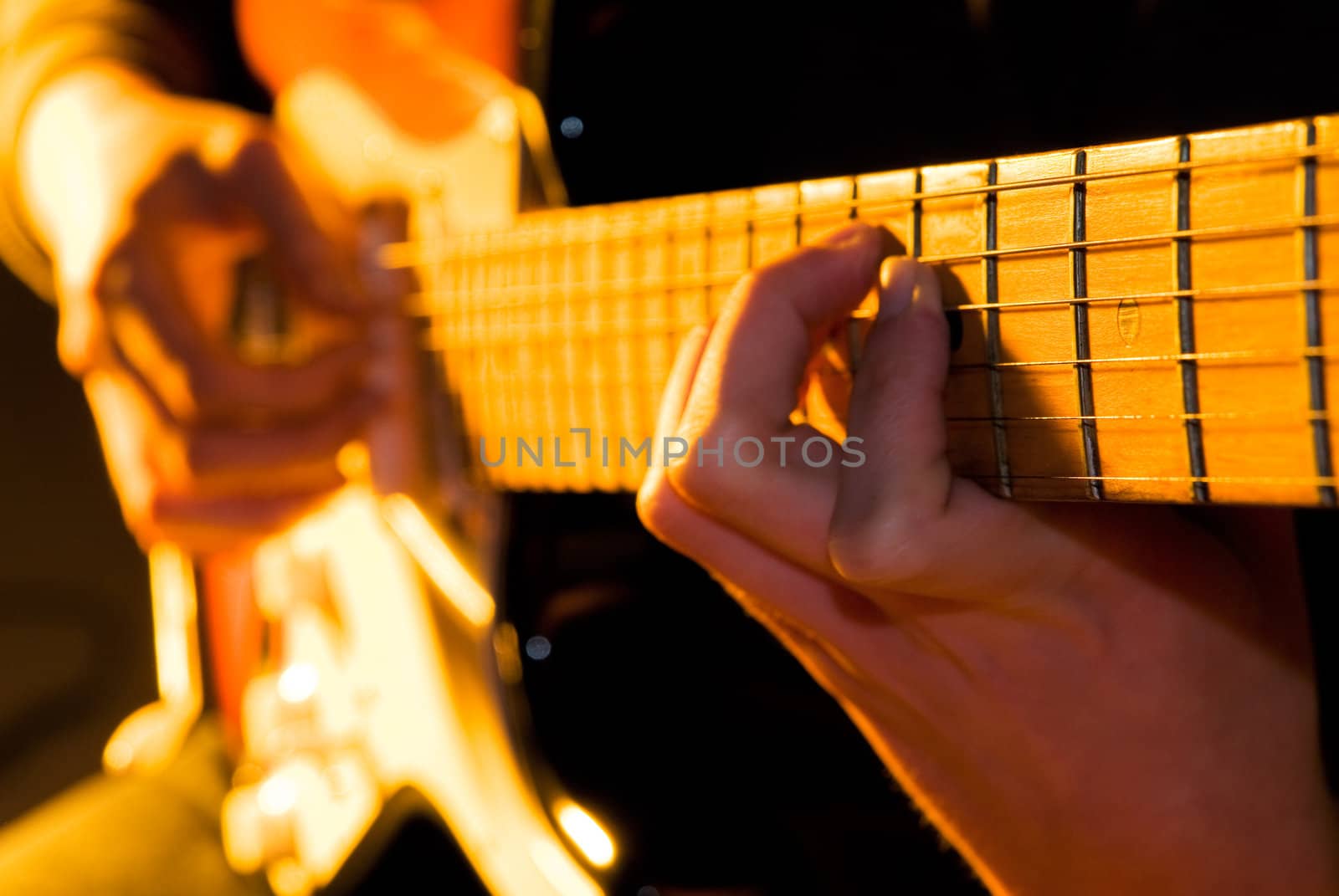 Hand playing guitar chord with shallow depth of field and orange lighting. 