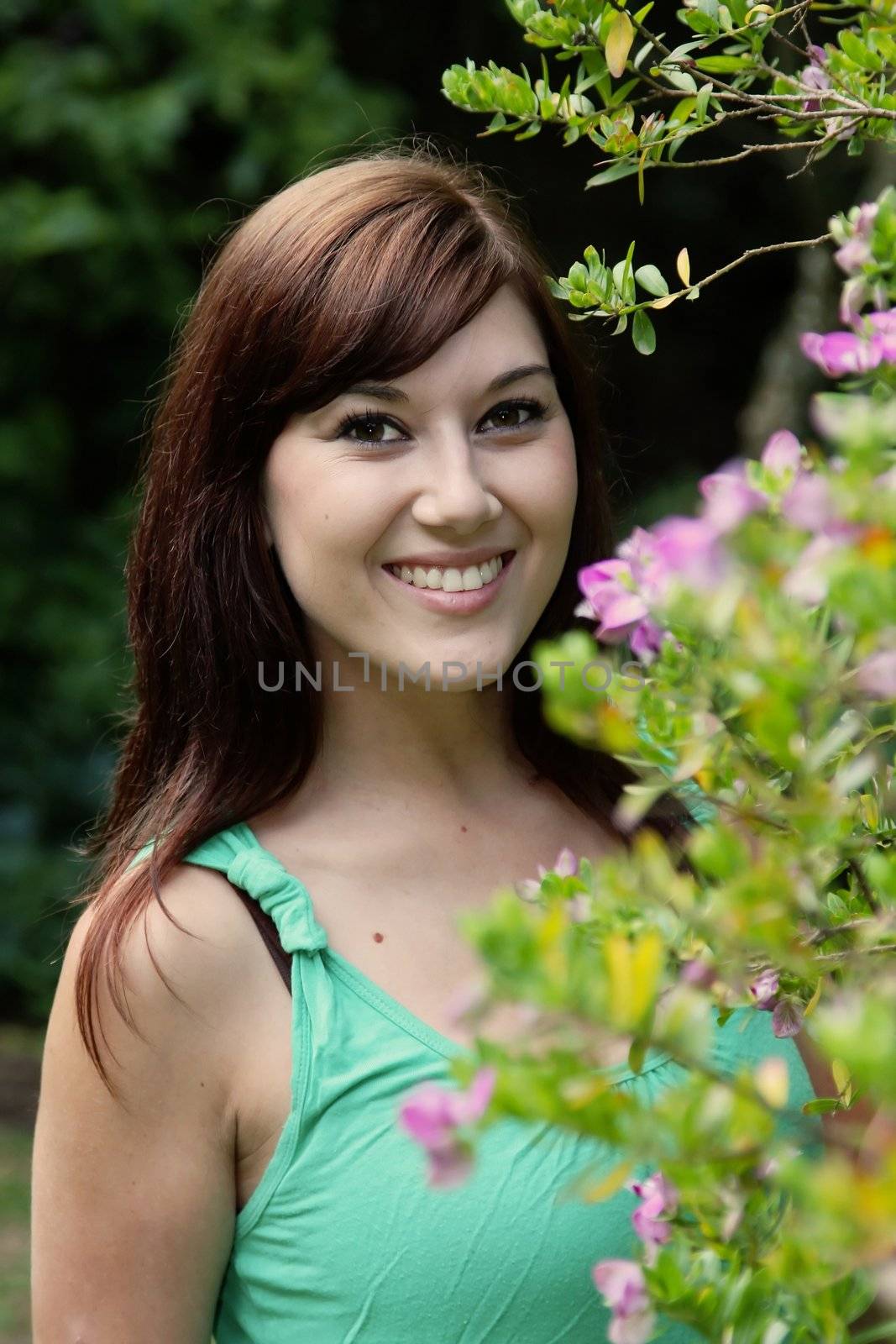 Pretty girl with beautful smile standing outdoors next to flowering bush