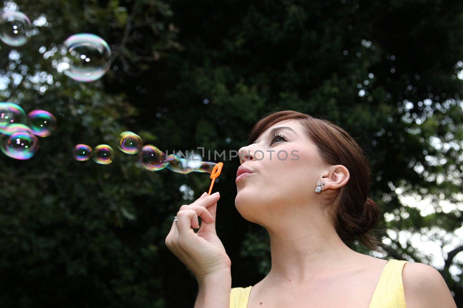 Pretty young woman blowing soap bubbles outdoors