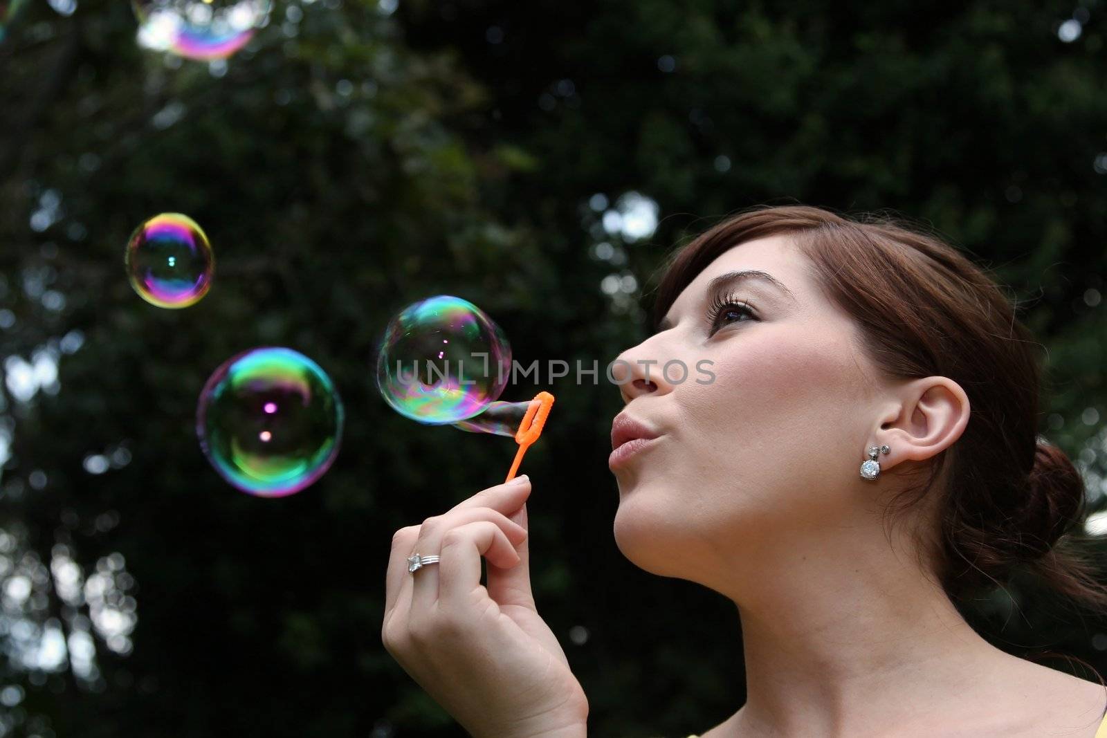 Pretty young woman blowing soap bubbles outdoors