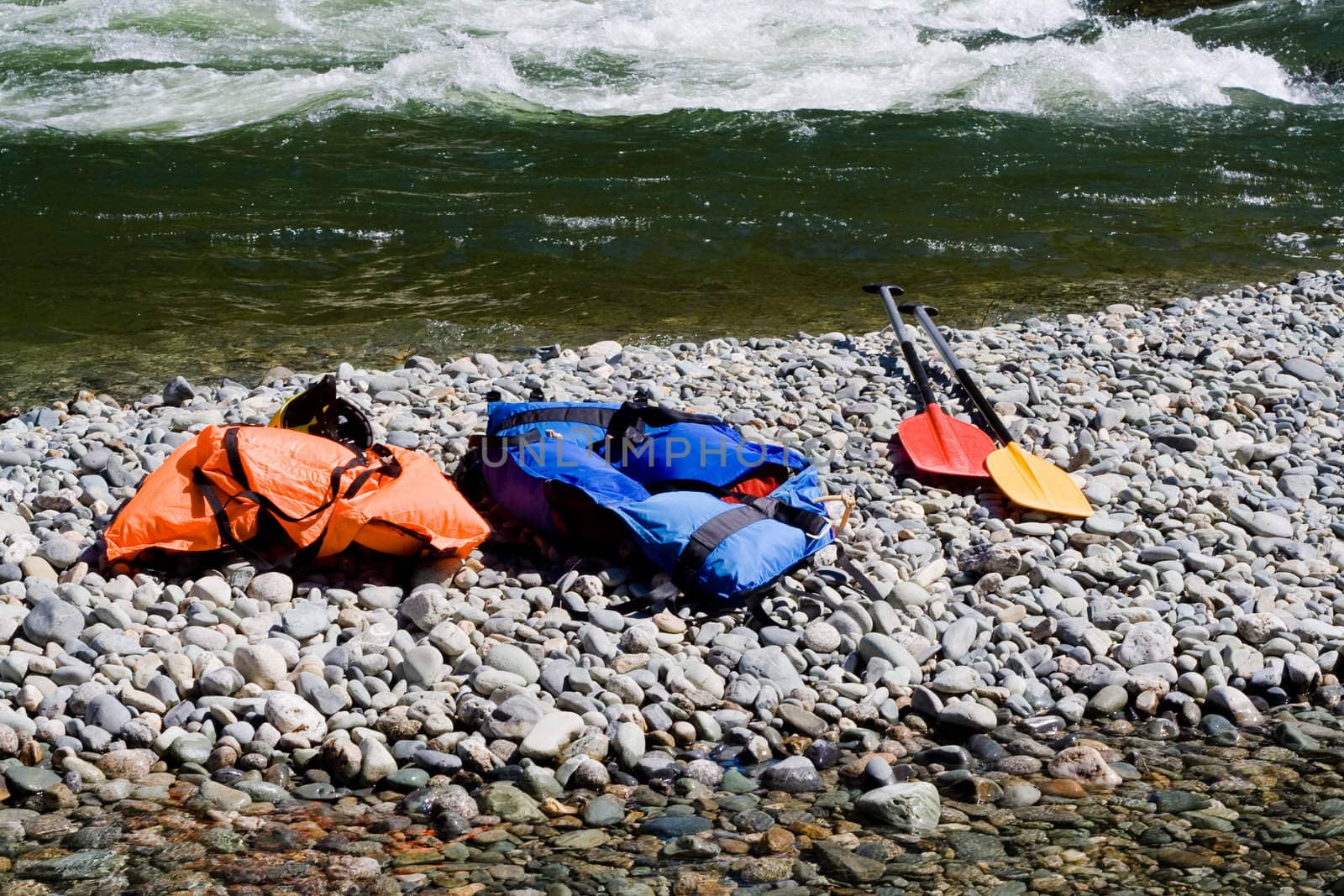 two  life-jackets and two paddles near river
