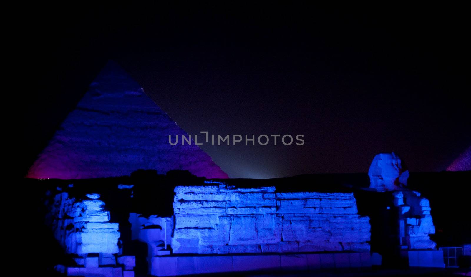 Giza Pyramids and sphinx illuminated by colored lights at night