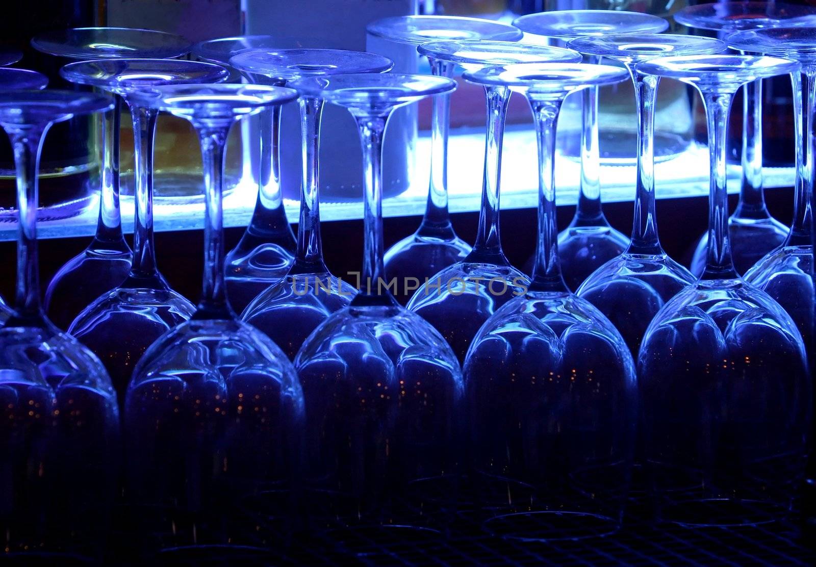 Wine glasses backlit with blue light and bottles in the background