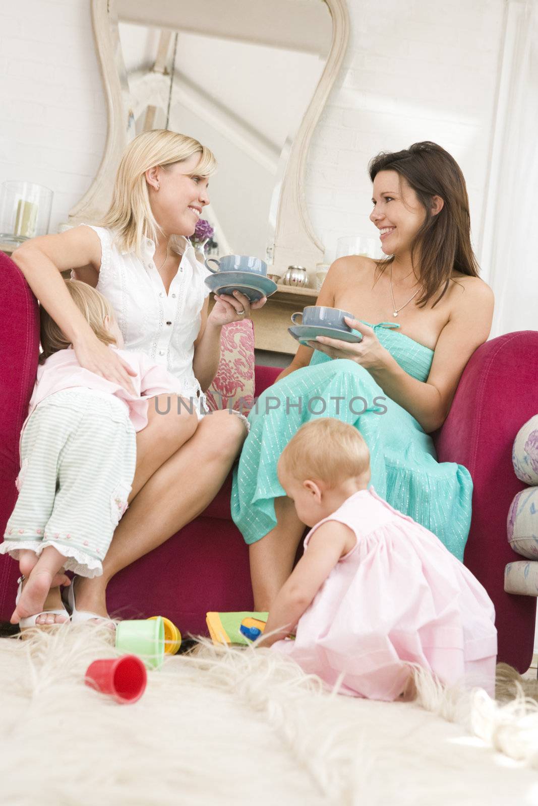 Two mothers in living room with babies and coffee smiling by MonkeyBusiness