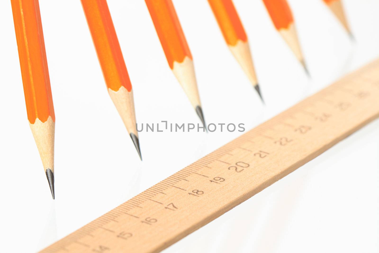 Few wooden yellow pencils in a row and ruler on white background