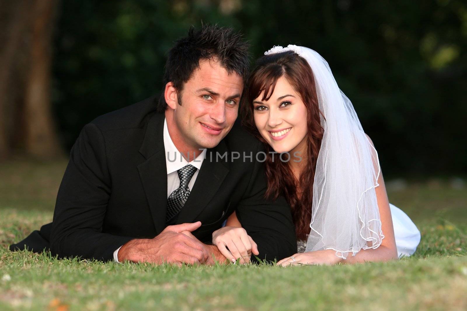 Beautiful wedding couple laying down outdoors on the grass
