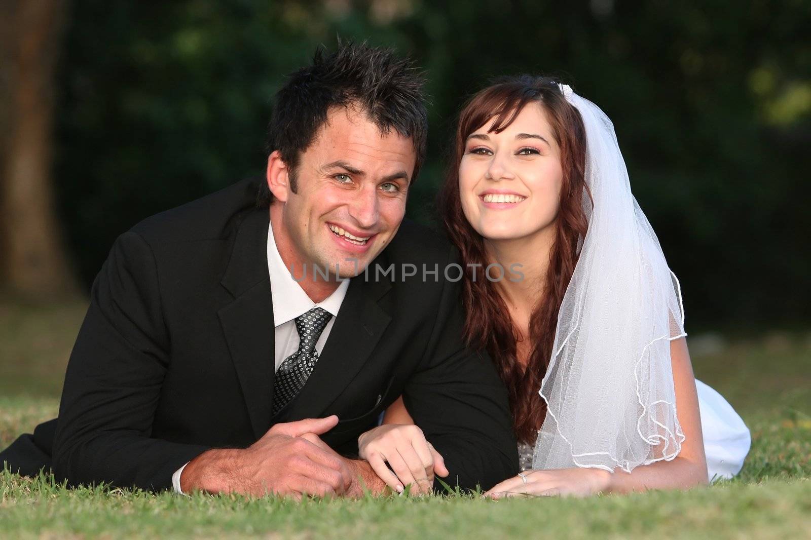 Beautiful smiling wedding couple laying down outdoors on the grass