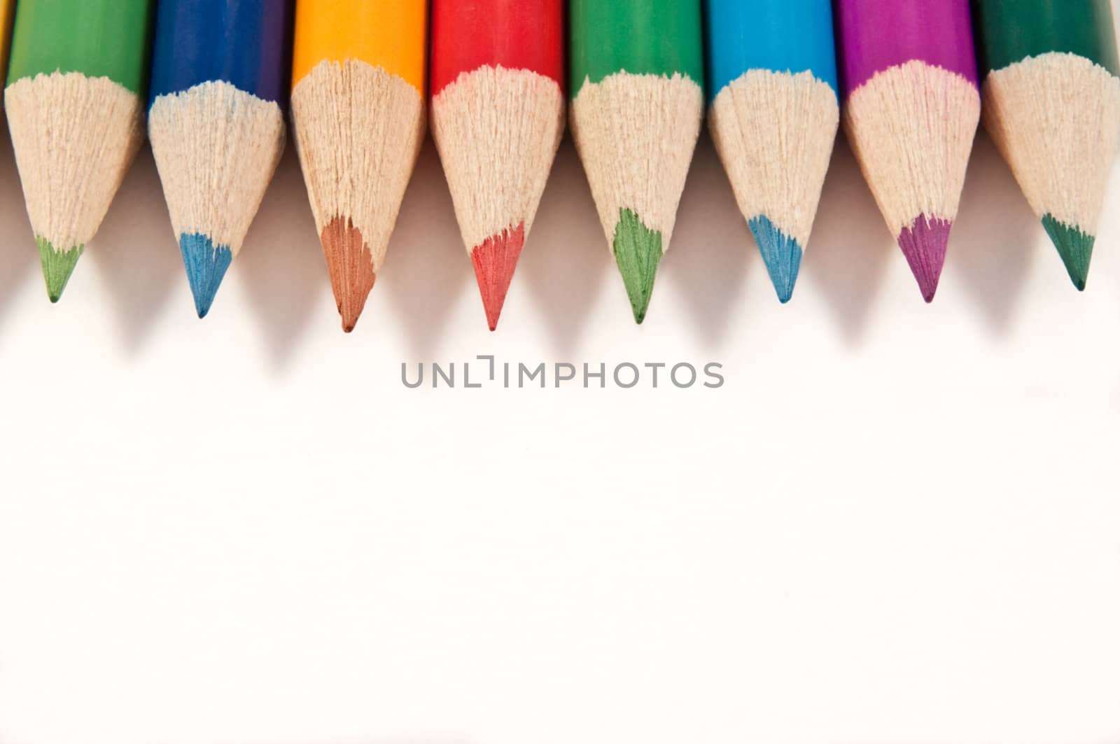 Close up capturing a selection of coloured drawing pencils arranged over white.