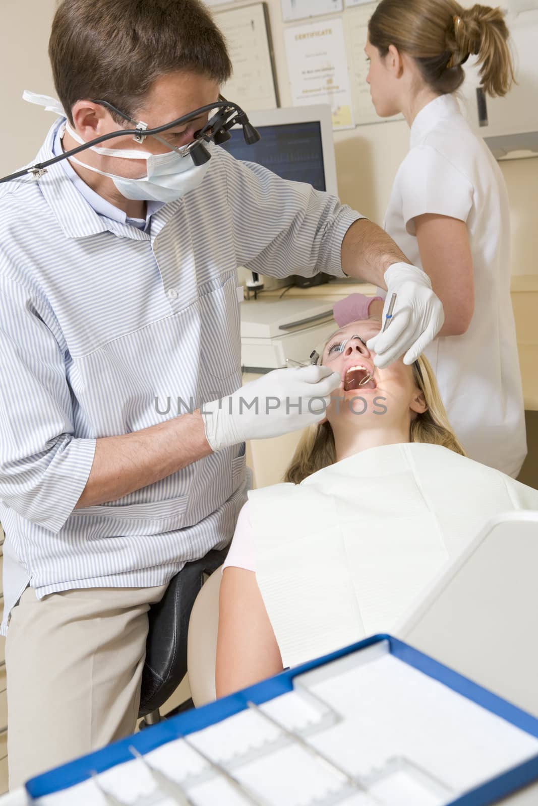 Dentist and assistant in exam room with woman in chair by MonkeyBusiness