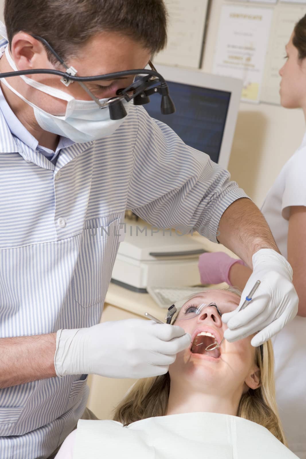 Dentist and assistant in exam room with woman in chair by MonkeyBusiness