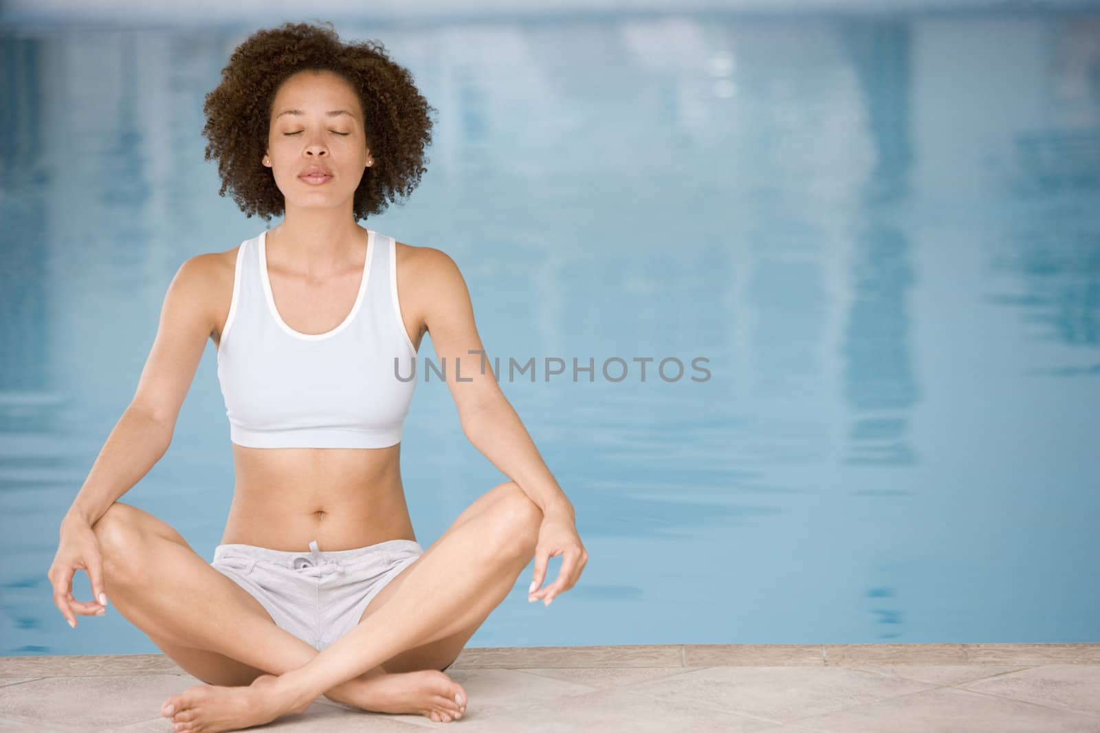 Woman sitting poolside doing yoga by MonkeyBusiness