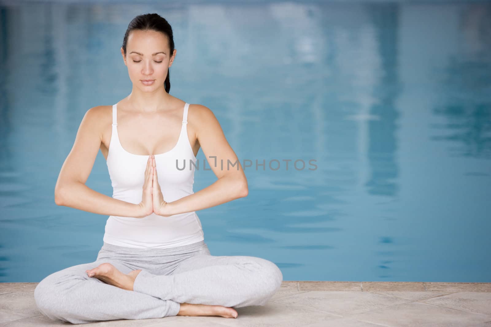 Woman sitting poolside doing yoga by MonkeyBusiness