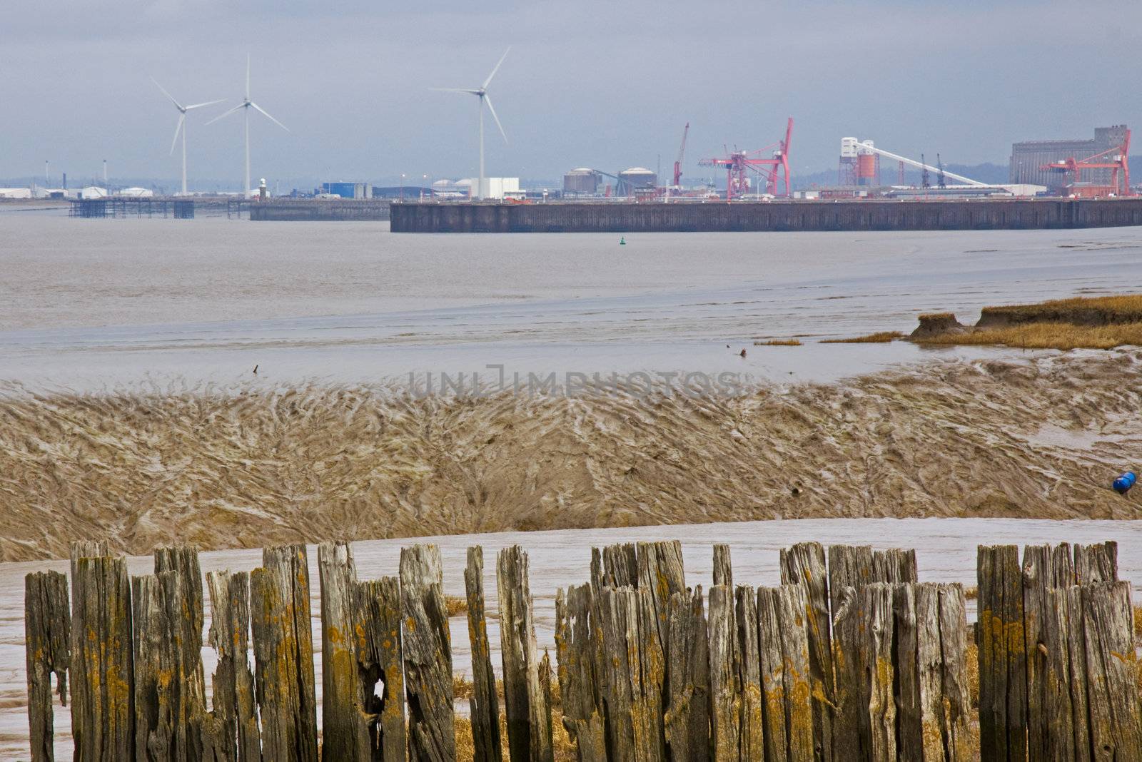 Rotten pier timbers at Portishead with the cranes and wind turbines at Avonmouth docks on the horizon
