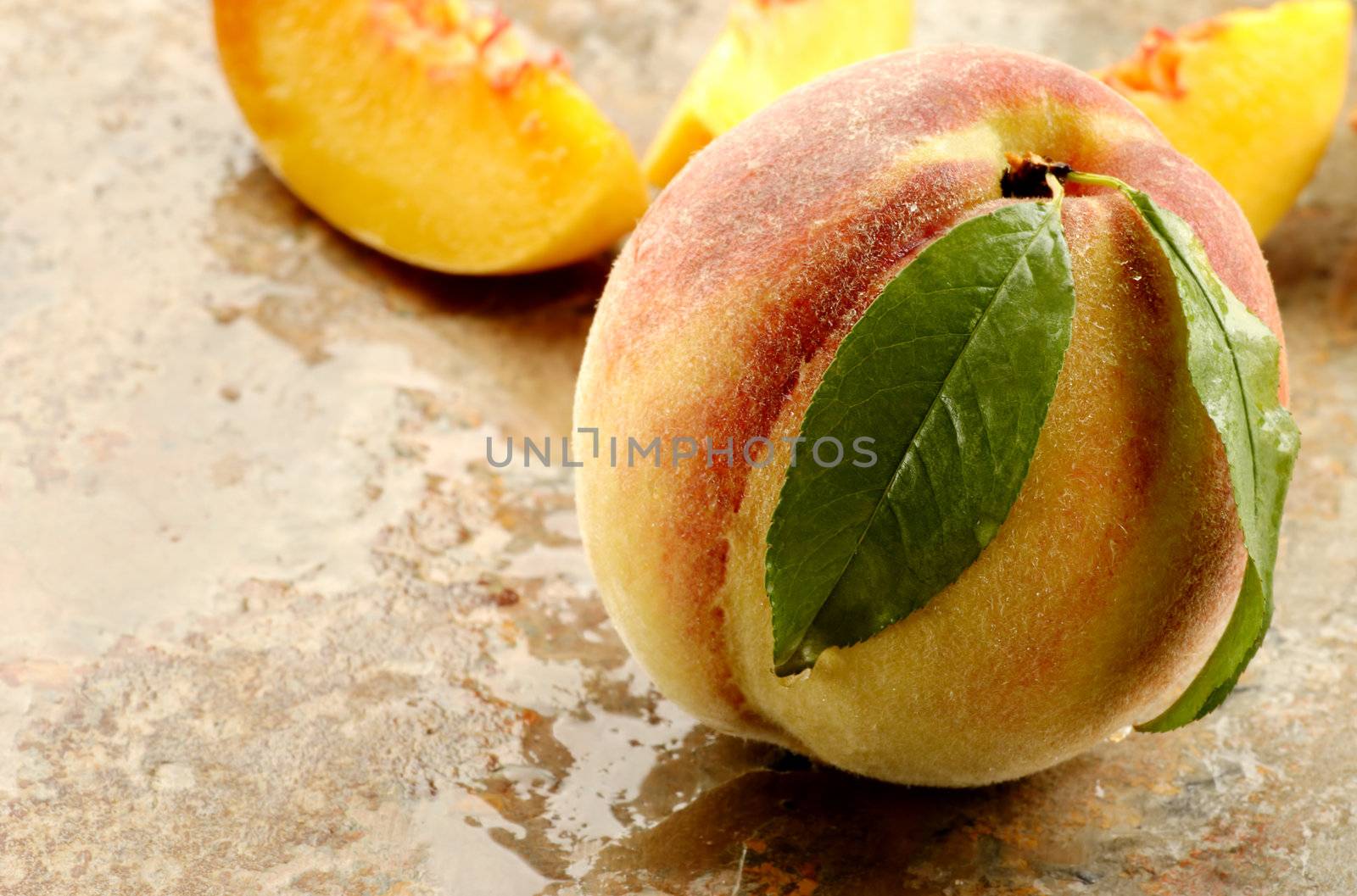 Whole and sliced fresh picked peach on a stone counter.