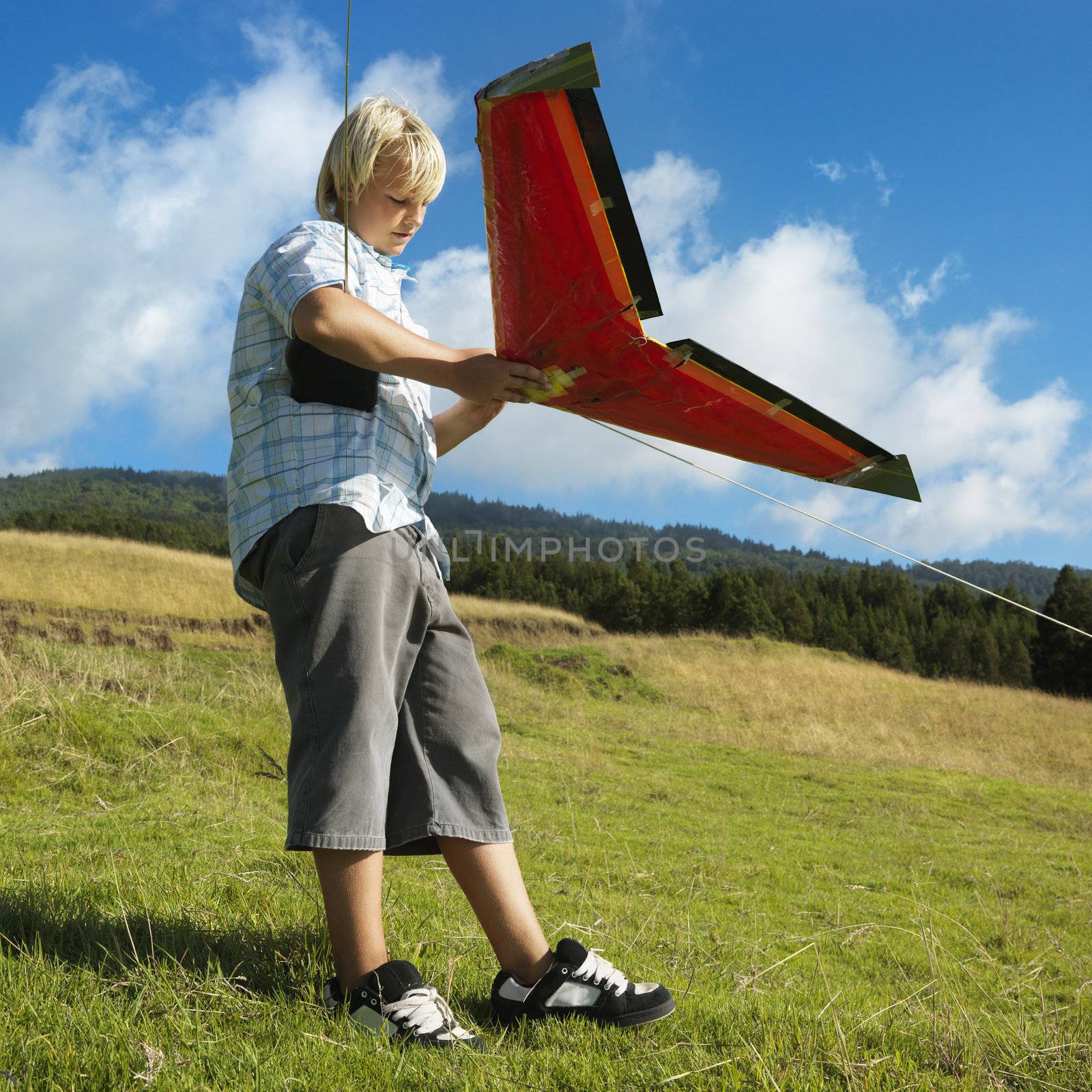 Pre-teen Caucasian male preparing to fly remote controlled airplane on grassy knoll.