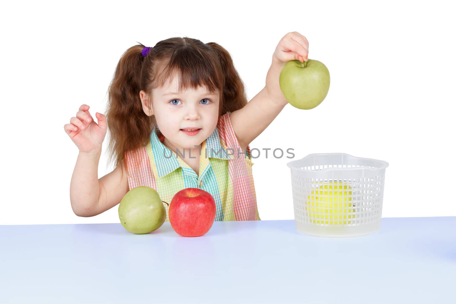 A little girl playing with green apples sitting at the table