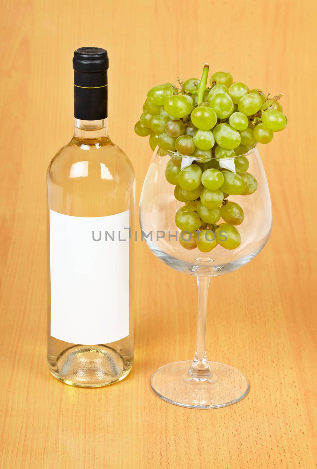 A bottle of wine, a large glass and grapes on wooden background