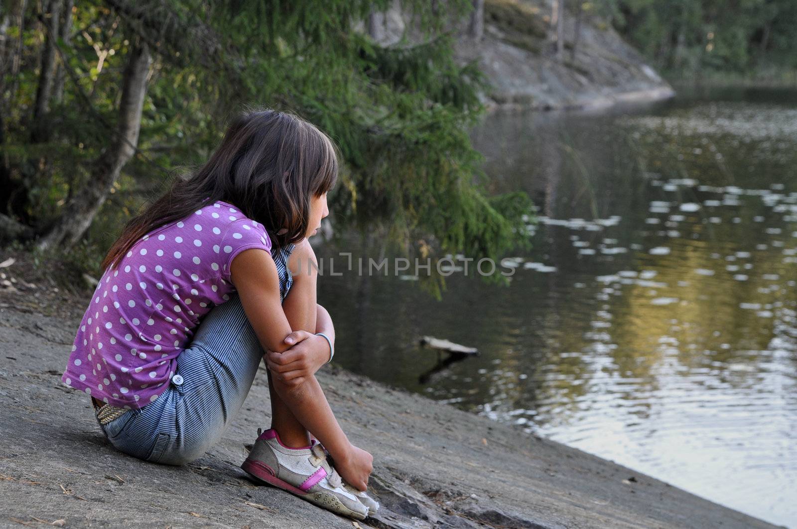 A contemplating girl sitting by a calm lake in Sweden.