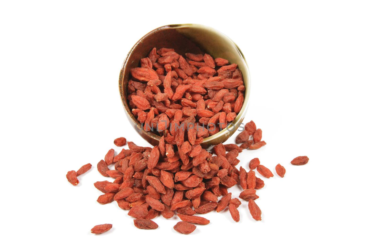 Red dry goji berries spilling out of a green and brown dish on a reflective white background