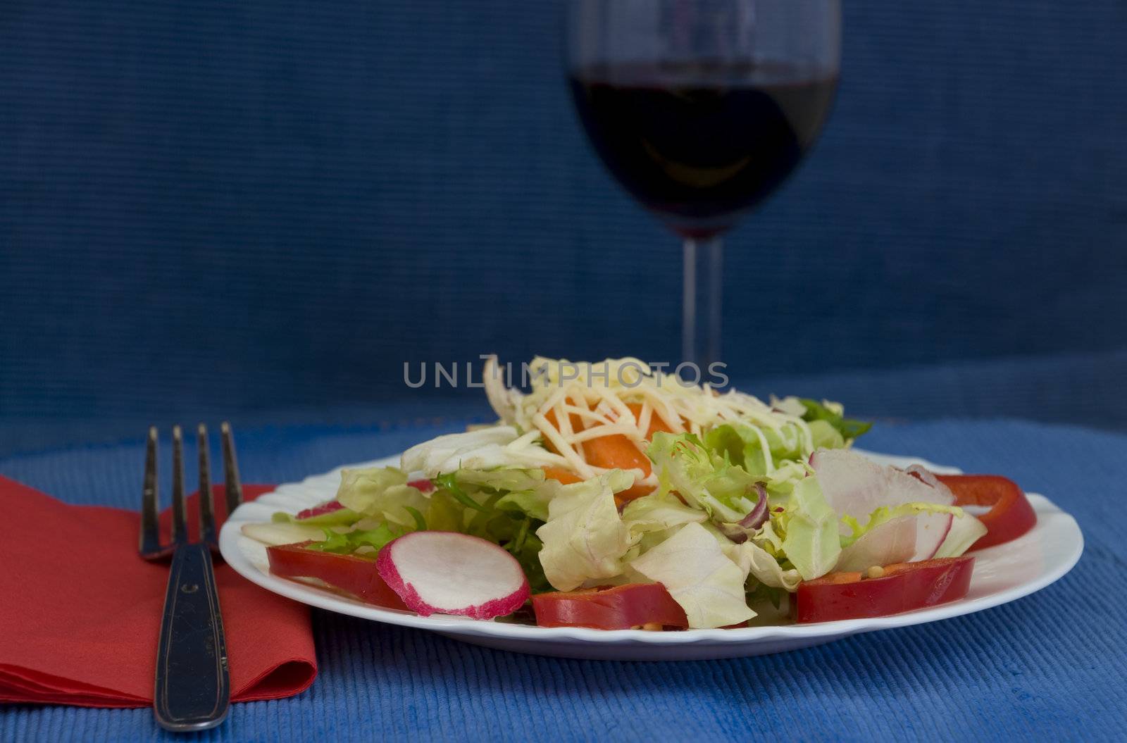 simple dinner setting for one with light salad and red wine, on blue background