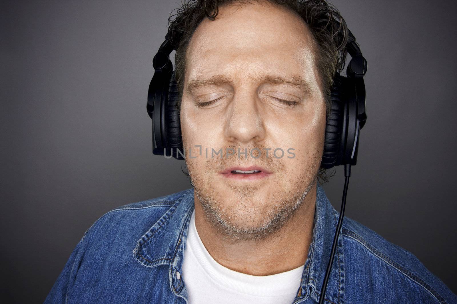 Man with Eyes Shut Wearing Headphones Enjoying His Music on a Grey Background.