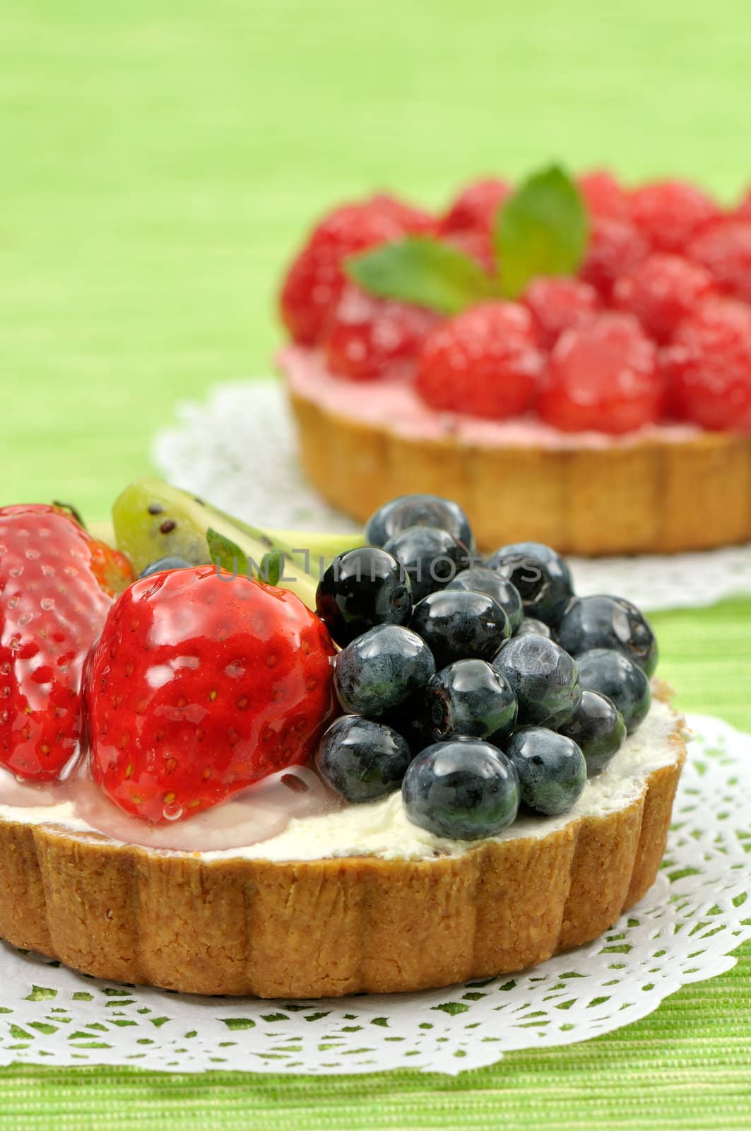 Assorted fruit tartlets on white doily and green background