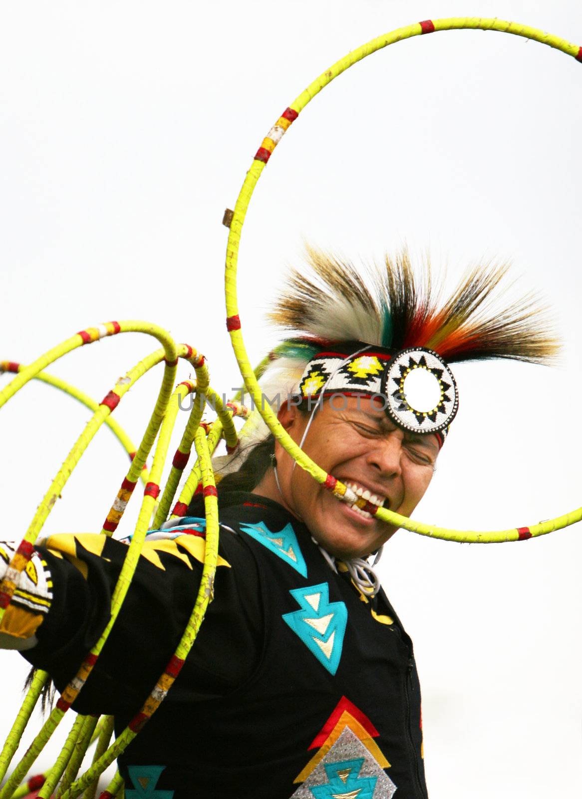 A Native American performs a traditional hoop dance. He is holding one ring in his mouth and has several more on his back.