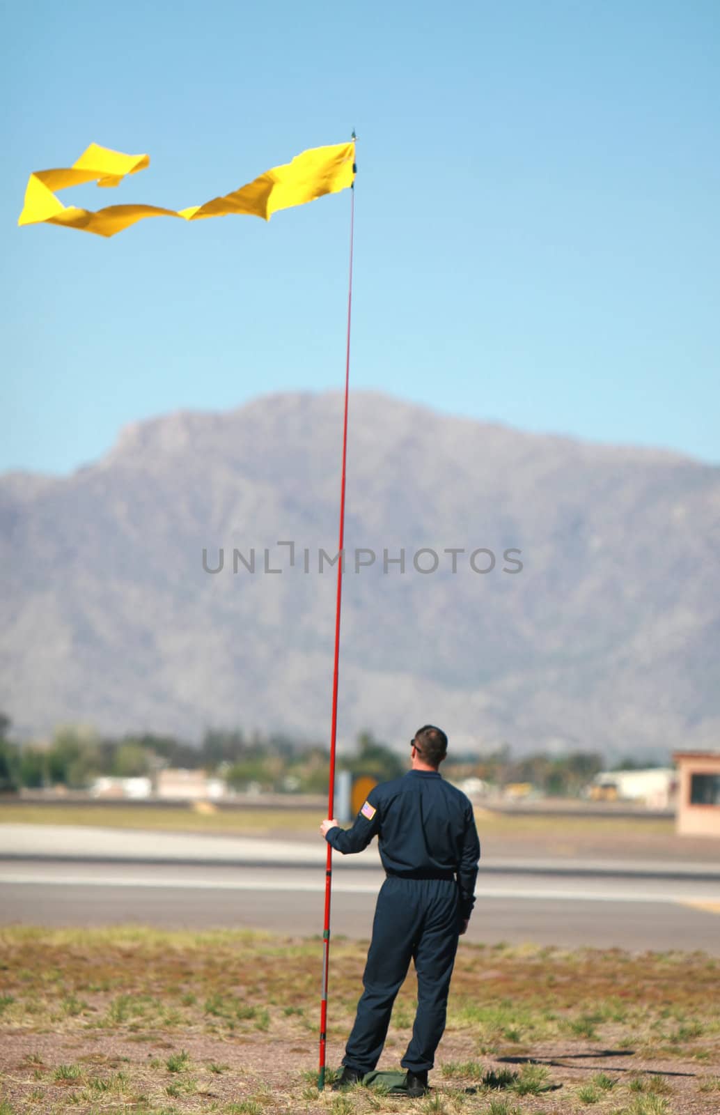 A flagman checks the wind direction so aid the landing of an airplane along an airstrip
