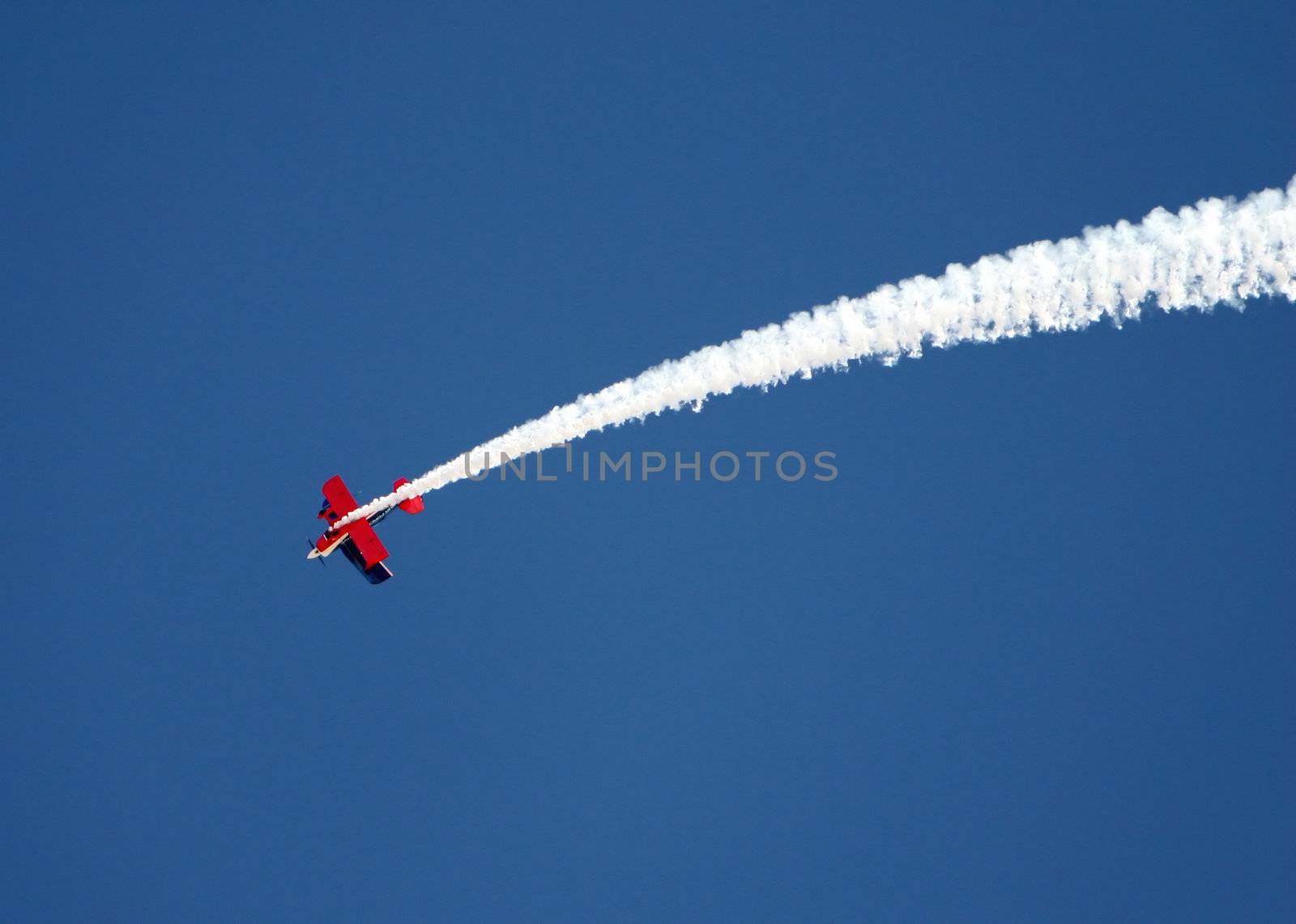 A stunt airplane performs a inverted roll at an airshow. Bright blue sky
