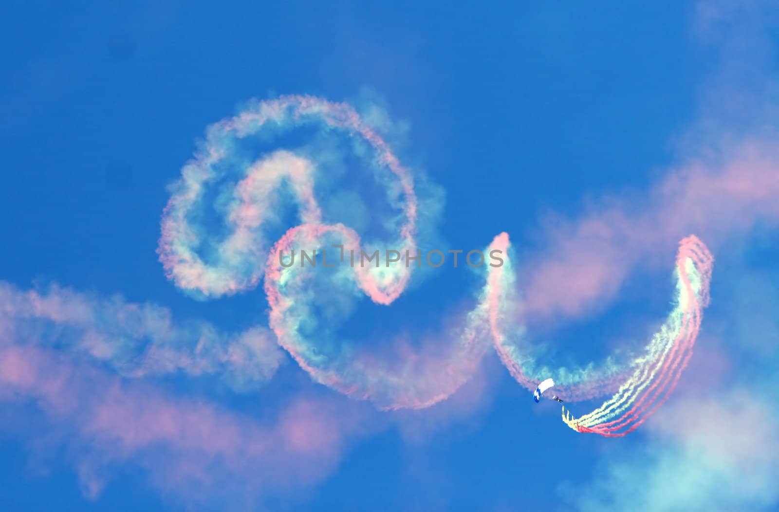 A parachute jumper with smoke canisters leaves a colorful trail in the blue sky
